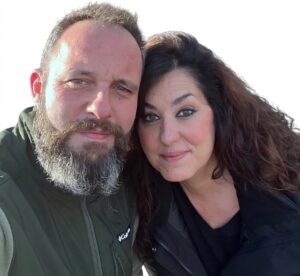Pareja sonriente en un entorno natural, representando su negocio de leña y carbón.