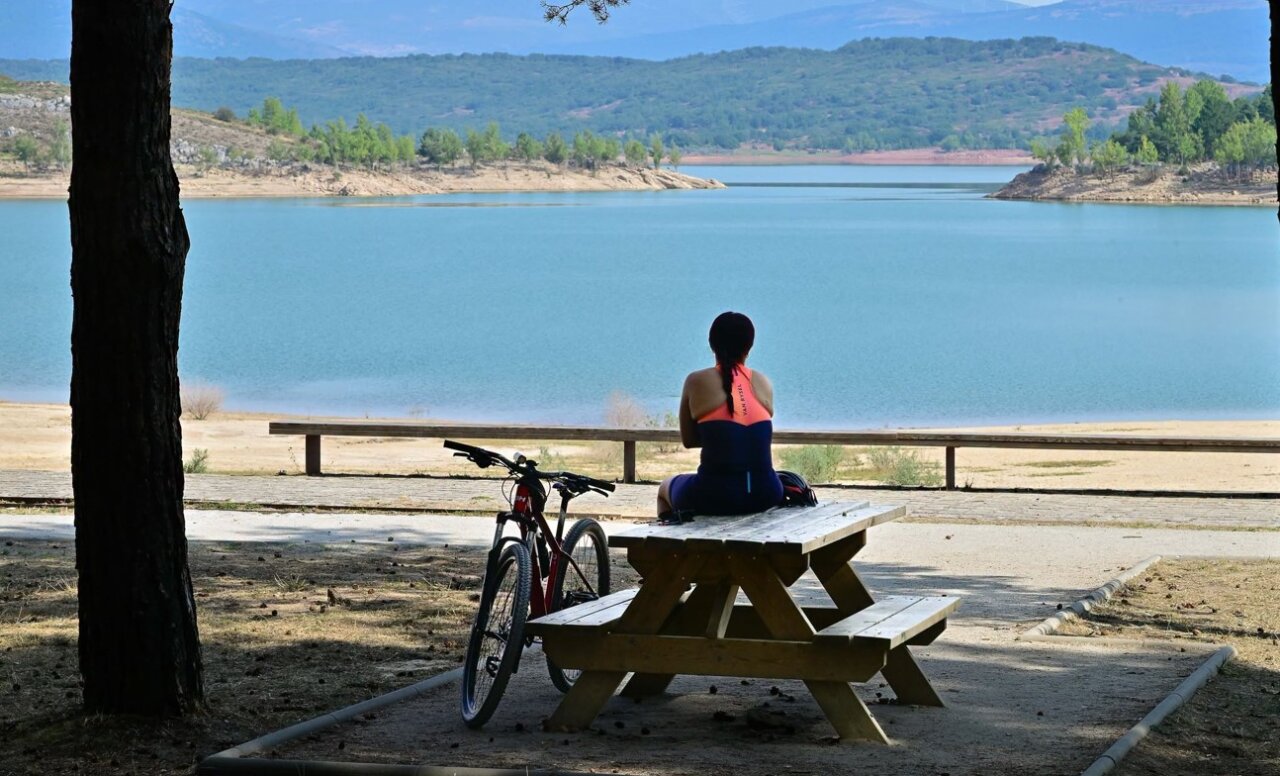 Persona sentada en un banco con una bicicleta junto a un embalse