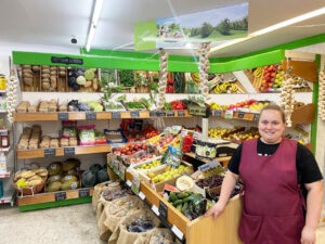 Interior del supermercado Axel y Luna con productos frescos y una empleada sonriendo.