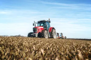 Tractor agrícola rojo trabajando en un campo cultivado bajo un cielo azul