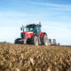Tractor agrícola rojo trabajando en un campo cultivado bajo un cielo azul