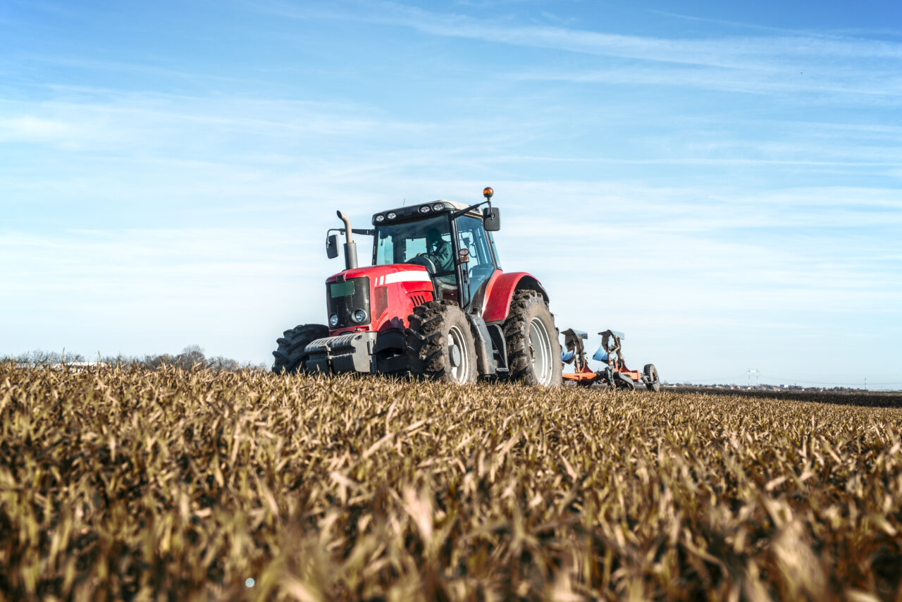 Tractor agrícola rojo trabajando en un campo cultivado bajo un cielo azul