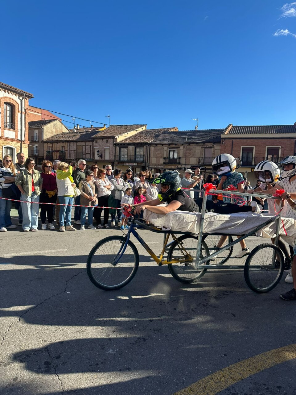 Participantes en la Carrera de Camas en Saldaña con disfraces y una cama sobre ruedas.
