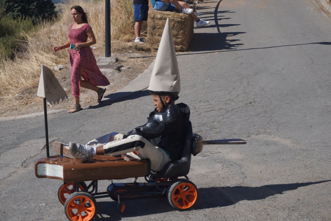 Niño en un vehículo improvisado con un sombrero en una carrera de autos locos.