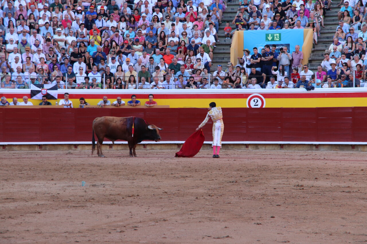 Torero realizando un pase con capa roja frente a un toro en la plaza de toros