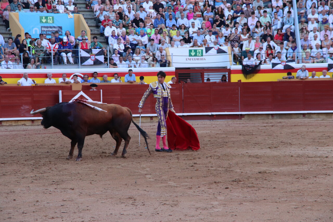 Torero en la plaza de toros de Palencia lidiando un toro con un capote rojo.