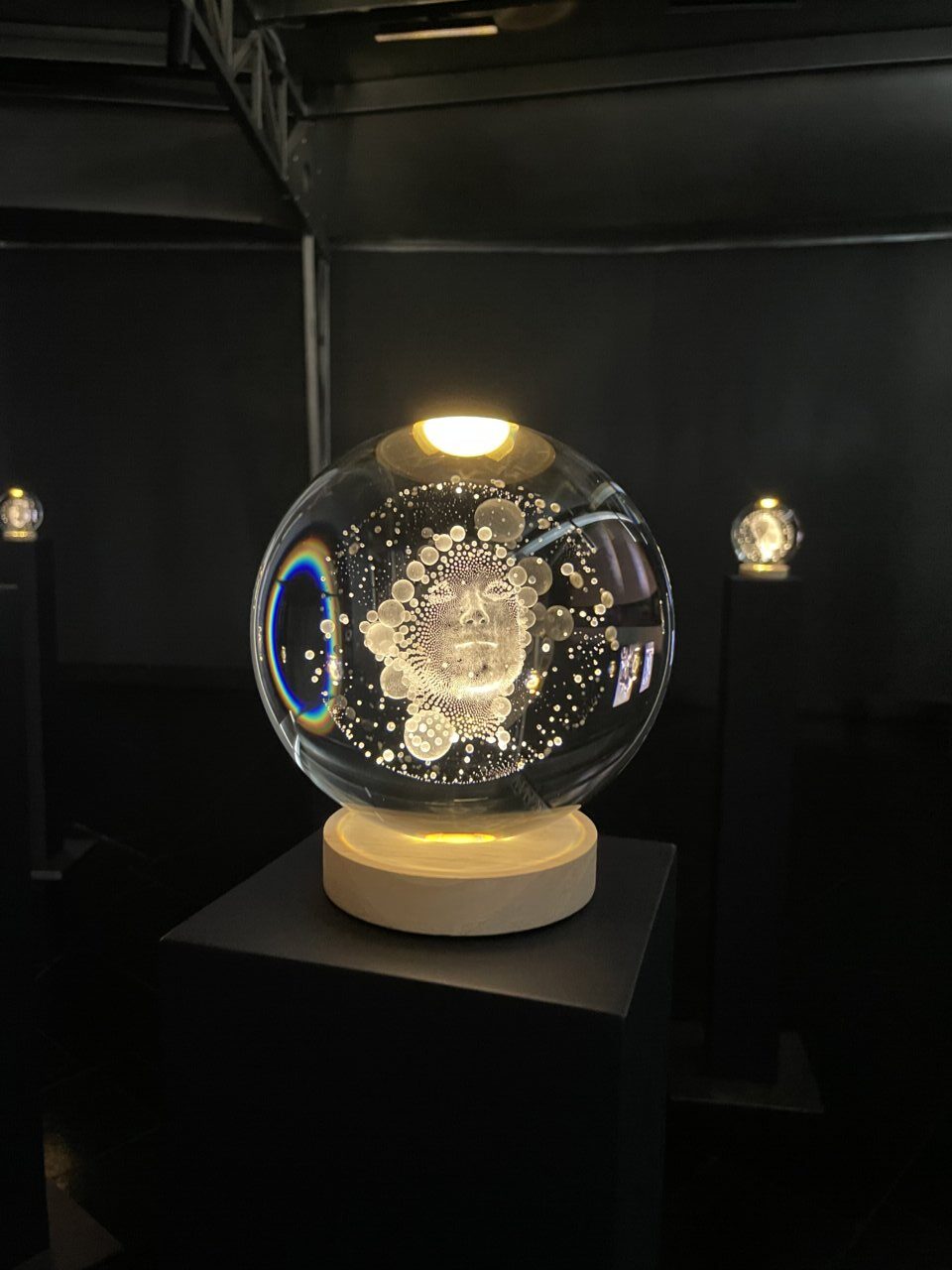 Esfera de cristal grabada con rostro humano en exposición de arte contemporáneo.