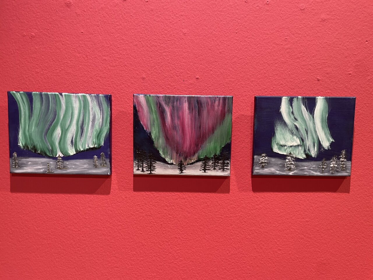 Tres cuadros que representan auroras boreales en colores vibrantes.