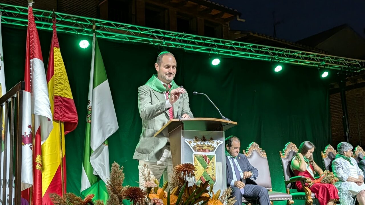 Un hombre dando un pregón en las fiestas de Saldaña con banderas al fondo