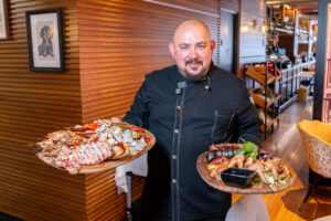 Chef Sergio Aguilar sosteniendo platos de parrilladas en un restaurante