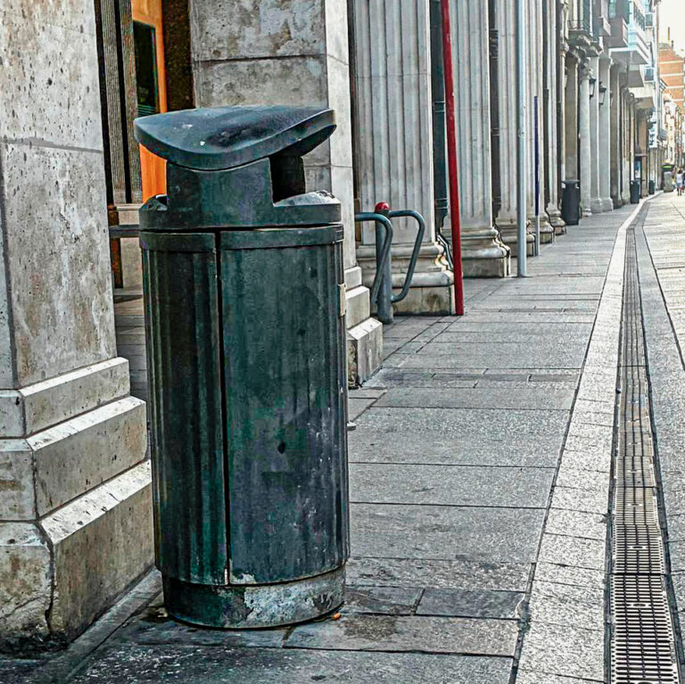 Papelera verde en una calle con pavimento de piedra