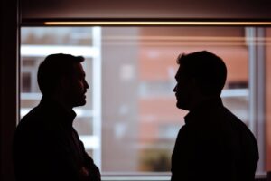Silhouette de dos hombres conversando junto a una ventana en un entorno urbano.