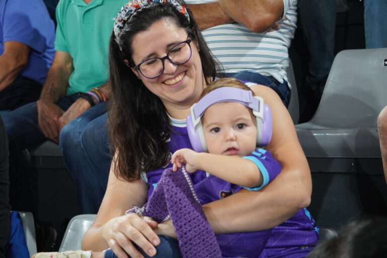 Mujer sonriente con un bebé en un partido de baloncesto