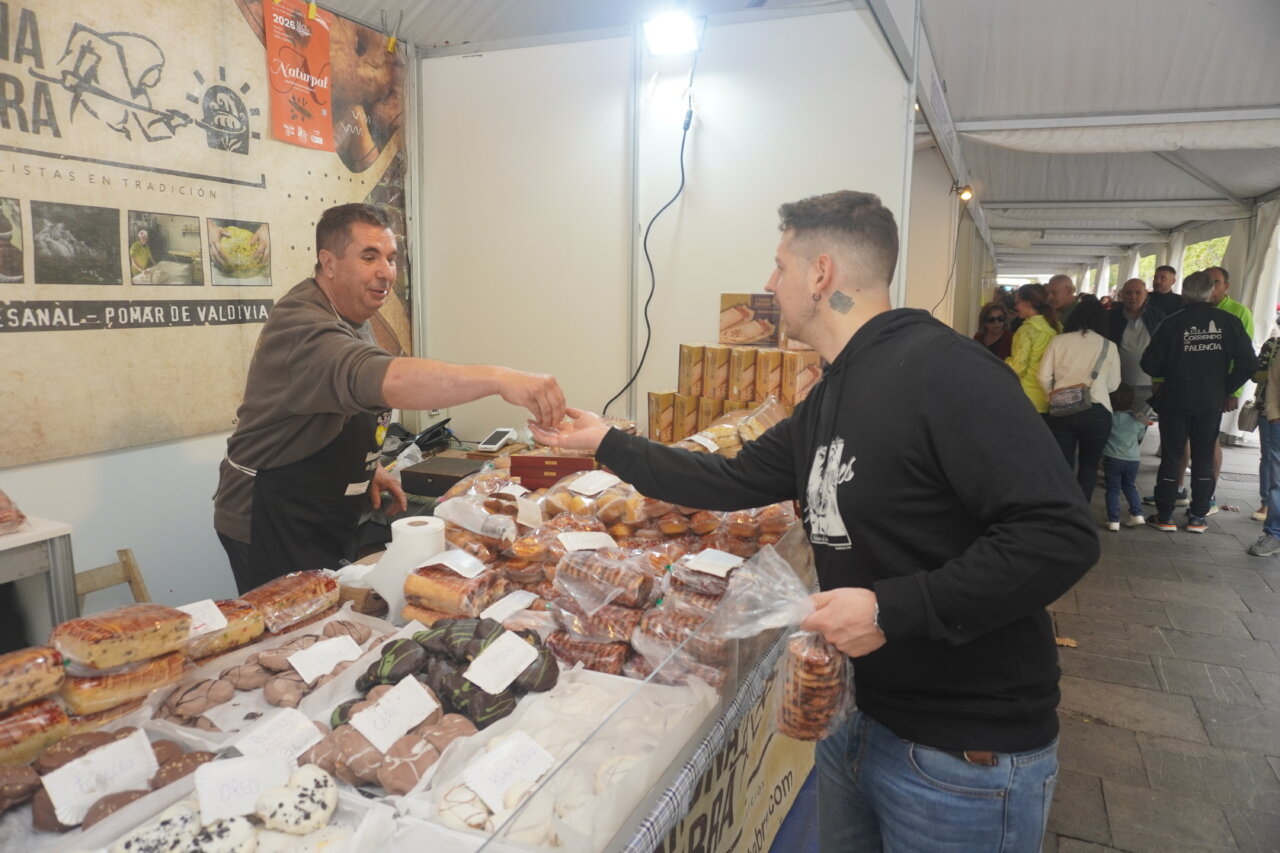 Dos hombres interactuando en un puesto de feria de productos cárnicos.