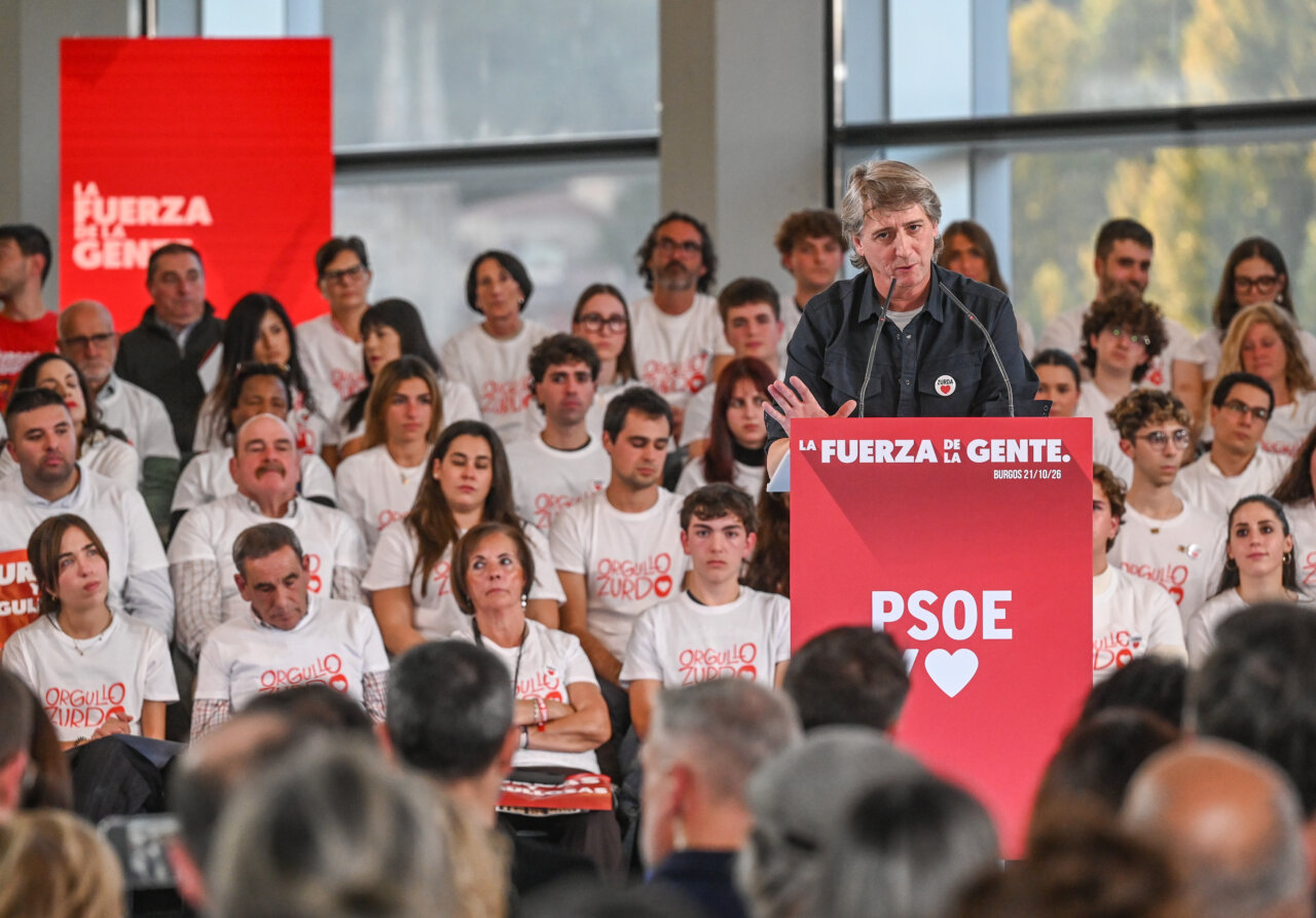 Un hombre habla desde un atril del PSOE ante un público con camisetas blancas.