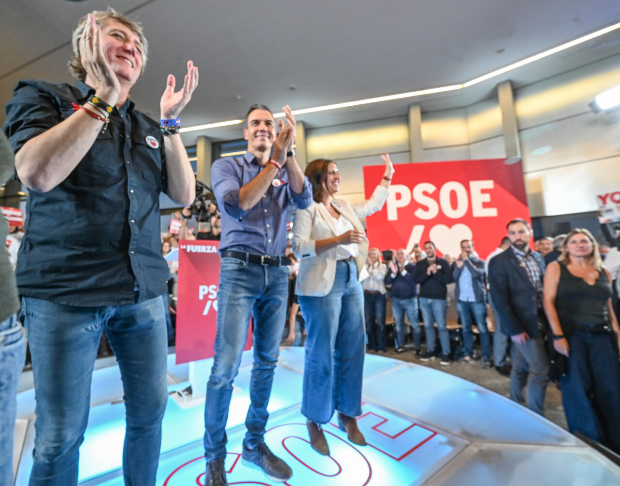 Varias personas aplauden sobre un escenario frente a una gran pancarta del PSOE