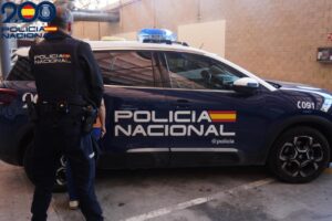 Agente de espaldas junto a un coche rotulado de la Policía Nacional en un interior.