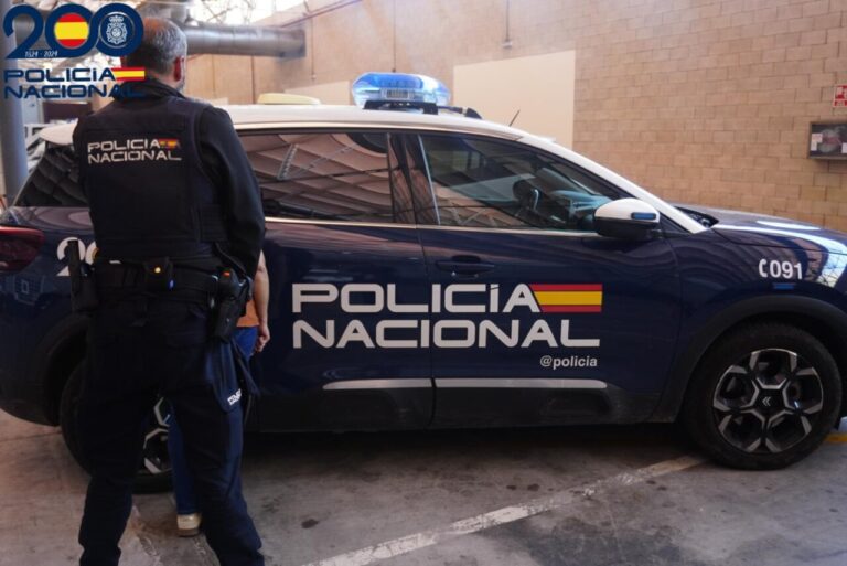 Agente de espaldas junto a un coche rotulado de la Policía Nacional en un interior.