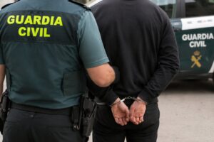 Agente de la Guardia Civil junto a una persona esposada frente a un vehículo policial.