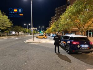 Agente de Policía Nacional junto a un coche patrulla en una calle iluminada de noche