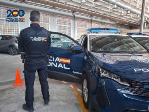 Agente de la Policía Nacional junto a un coche policial en un garaje.