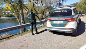 Agente de la Guardia Civil junto a un vehículo oficial en una carretera junto al agua