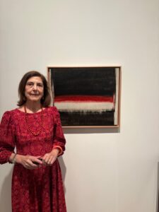 Mujer posa junto a un cuadro abstracto de franjas negras, rojas y blancas.