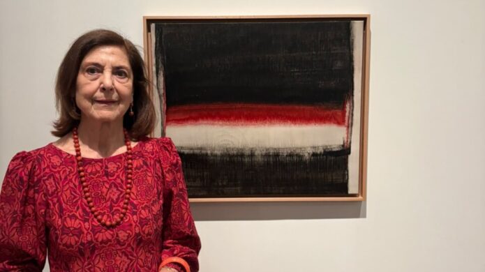 Mujer posa junto a un cuadro abstracto de franjas negras, rojas y blancas.