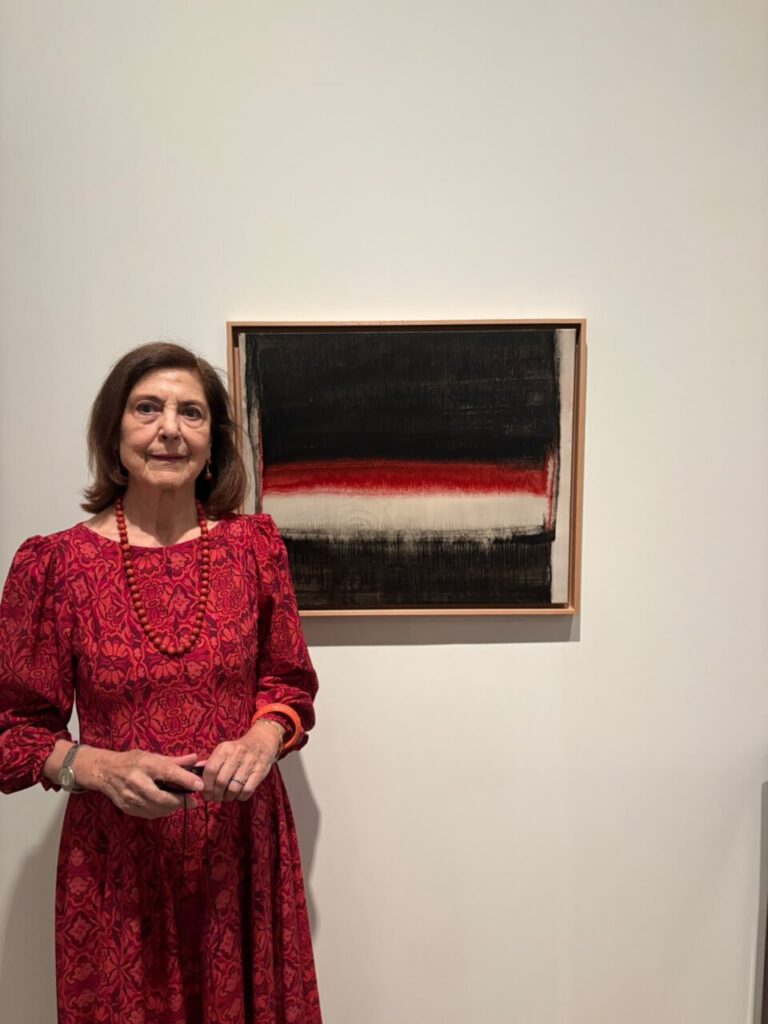 Mujer posa junto a un cuadro abstracto de franjas negras, rojas y blancas.