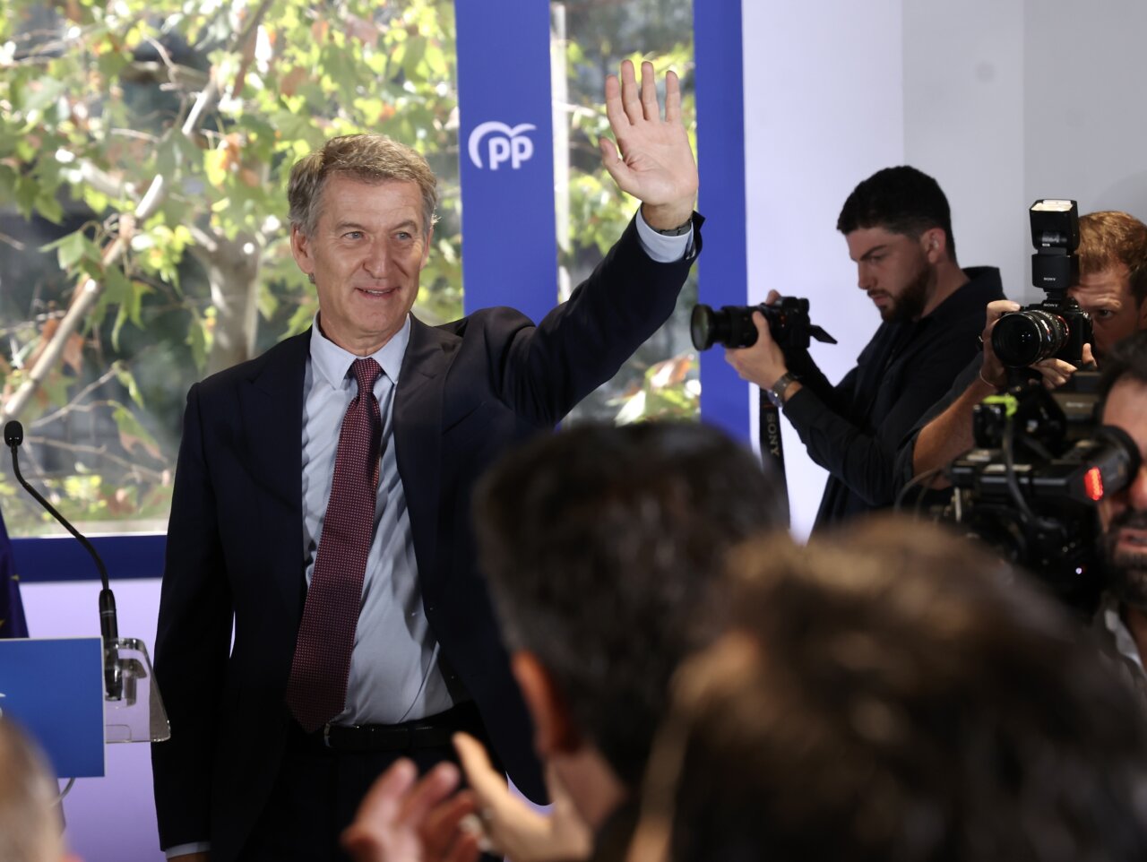 Alberto Núñez Feijóo saluda con la mano ante varias cámaras y un fondo del PP