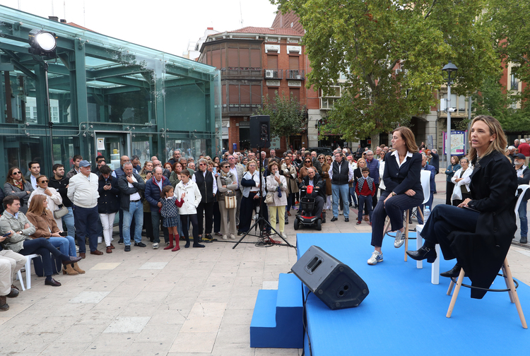 Dos mujeres sentadas en un escenario frente a un público reunido en una plaza.