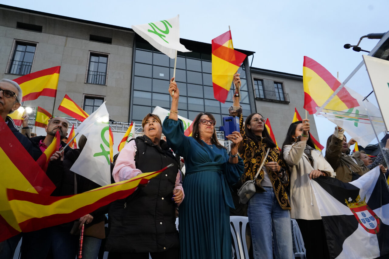 Asistentes sostienen banderas españolas y blancas durante un acto político al aire libre