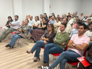 Asistentes sentados en filas de sillas rojas durante una reunión en una sala.