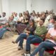 Asistentes sentados en filas de sillas rojas durante una reunión en una sala.
