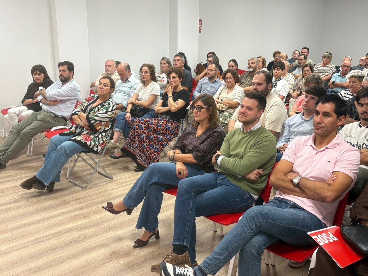 Asistentes sentados en filas de sillas rojas durante una reunión en una sala.