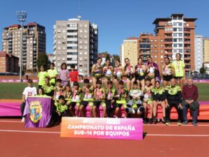 Grupo de jóvenes atletas posa con medallas en una pista junto al cartel del campeonato.