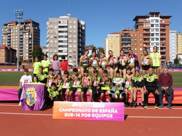 Grupo de jóvenes atletas posa con medallas en una pista junto al cartel del campeonato.
