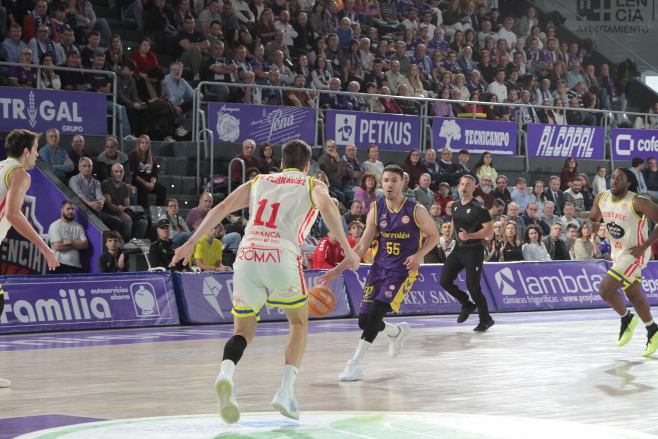 Un jugador de morado conduce el balón ante un rival de blanco en una cancha.