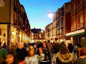 Personas pasean por la Calle Mayor de Palencia, entre edificios y comercios iluminados.