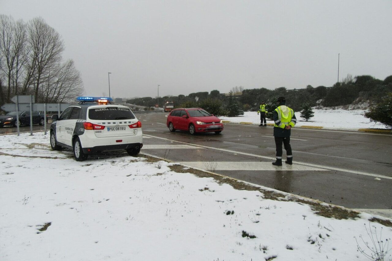 Coche de la Guardia Civil junto a agentes en una carretera nevada