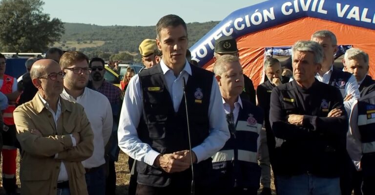 Un hombre habla ante un micrófono frente a una carpa de Protección Civil y varias personas.