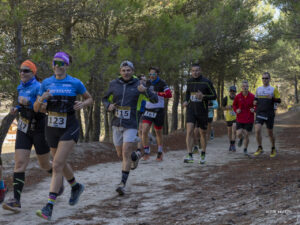 Corredores con dorsales avanzan por un sendero de tierra entre árboles.