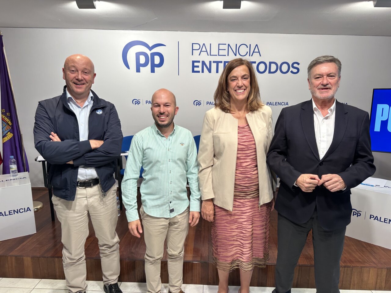 Cuatro personas posan frente a un panel del PP con referencias a Palencia.