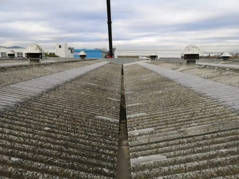 Cubierta ondulada de gran extensión con respiraderos y edificios al fondo.