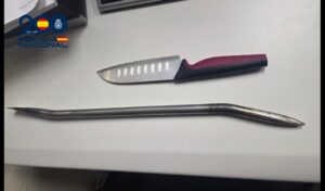 Un cuchillo de cocina y una barra metálica alargada sobre una mesa blanca.