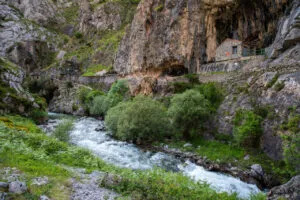 Río de aguas rápidas bajo un desfiladero rocoso con vegetación y construcciones de piedra