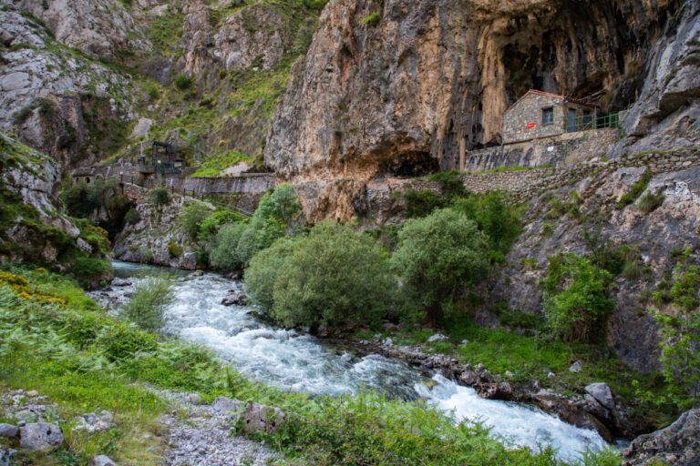 Río de aguas rápidas bajo un desfiladero rocoso con vegetación y construcciones de piedra
