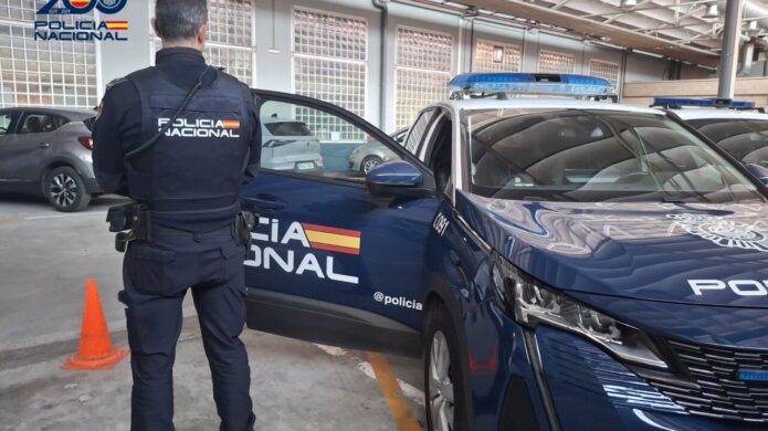 Agente de la Policía Nacional junto a un vehículo policial en un aparcamiento.