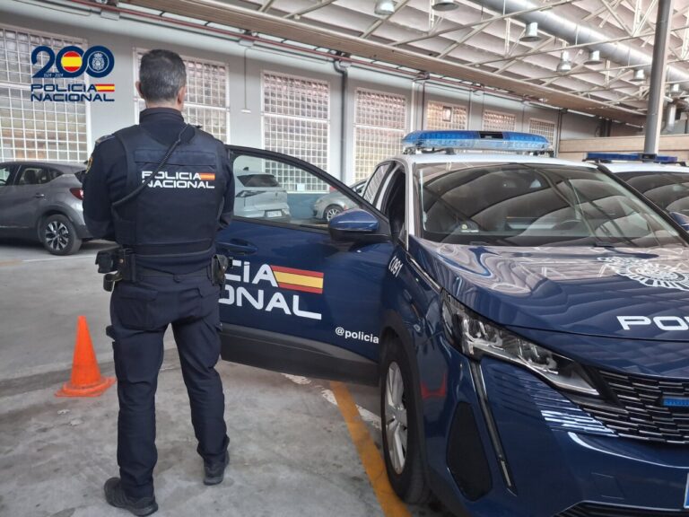 Agente de la Policía Nacional junto a un vehículo policial en un aparcamiento.