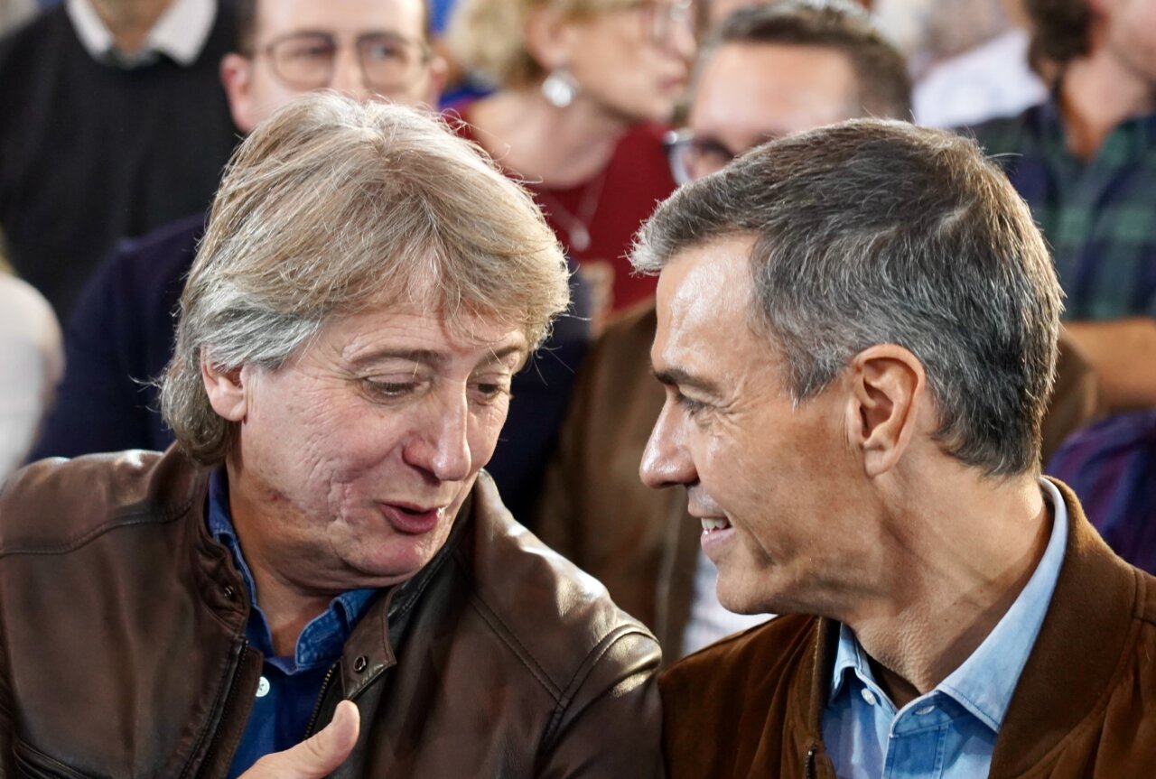 Fotografía de dos hombres conversando frente a un público desenfocado